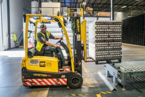 Warehouse worker operating a forklift, transporting labeled products, showcasing the benefits of using certified Zebra print supplies for efficient operations.